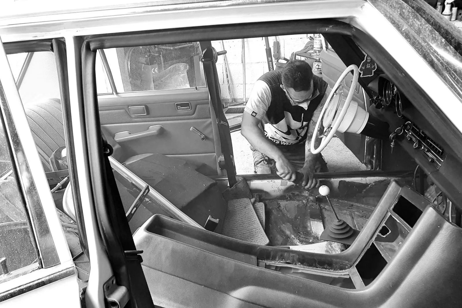 Schwarzweiß-Aufnahme: eine Person arbeitet im ausgebauten Innenraum eines Fahrzeugs am Mitteltunnel